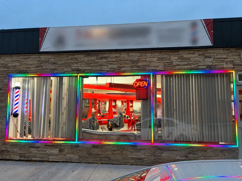 Real barbershop storefront with colourful LED strips around three windows; customer identifiers and people blurred