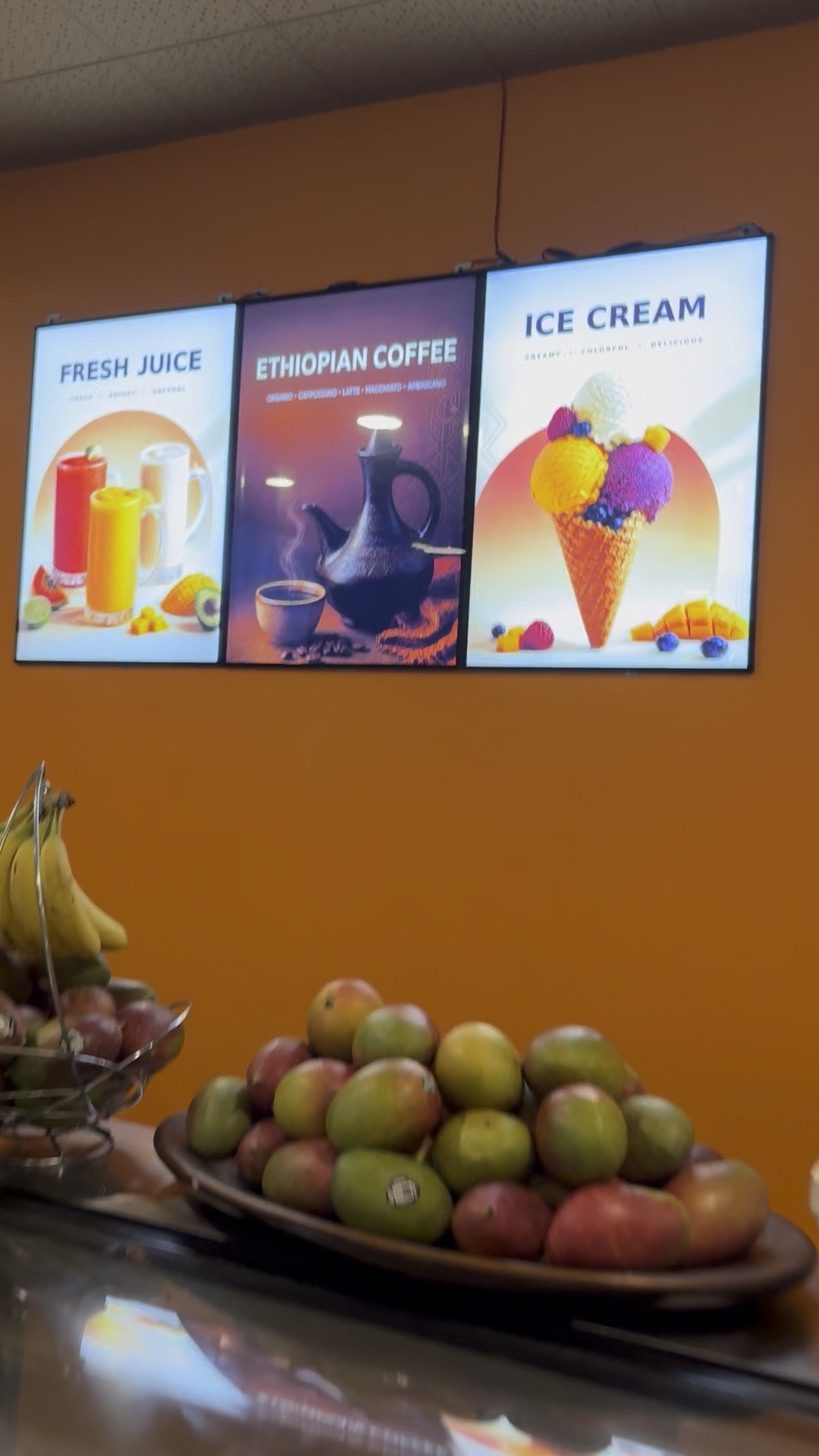 Three illuminated juice, Ethiopian coffee and ice cream lightboxes installed on an orange wall in a Calgary juice bar