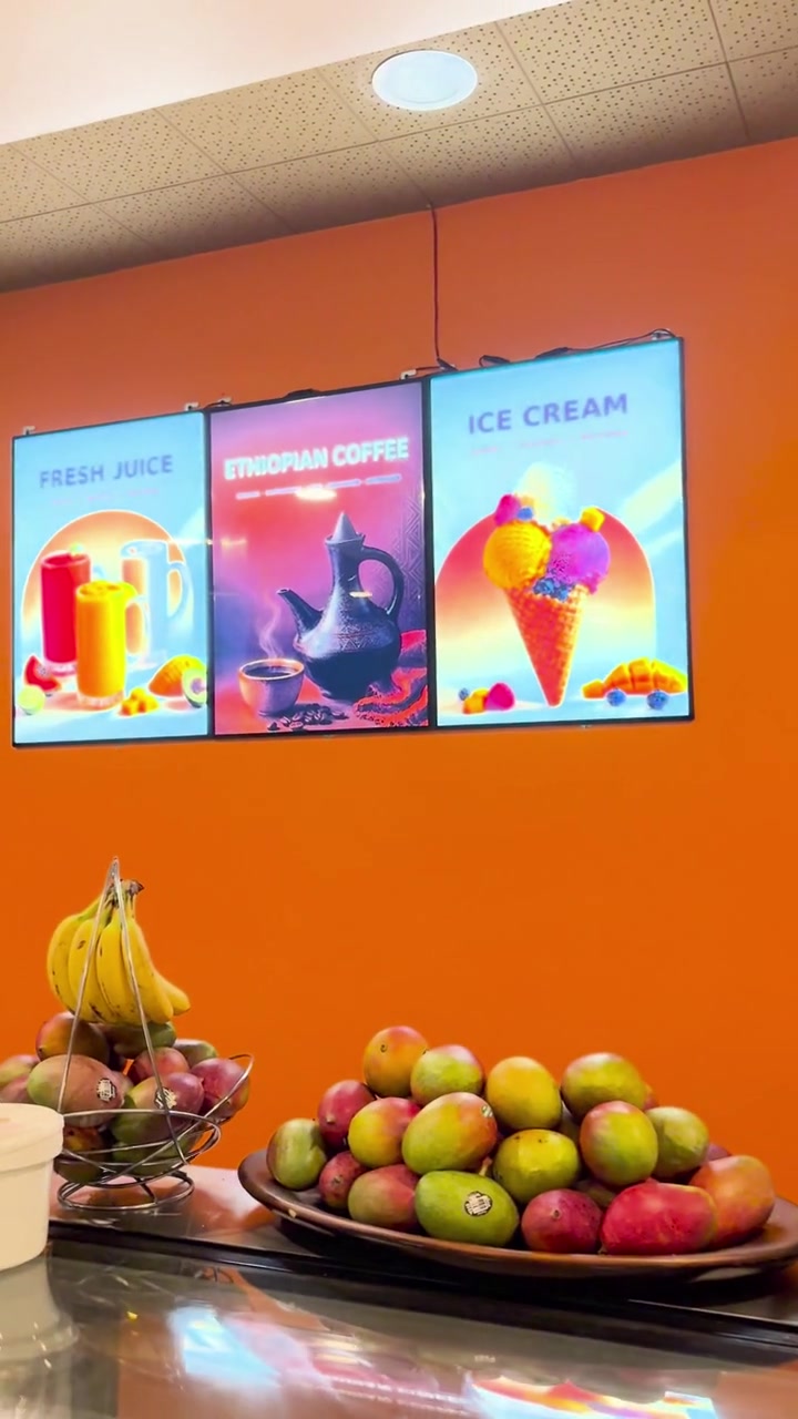 Three illuminated juice, Ethiopian coffee and ice cream lightboxes installed on an orange wall in a Calgary juice bar