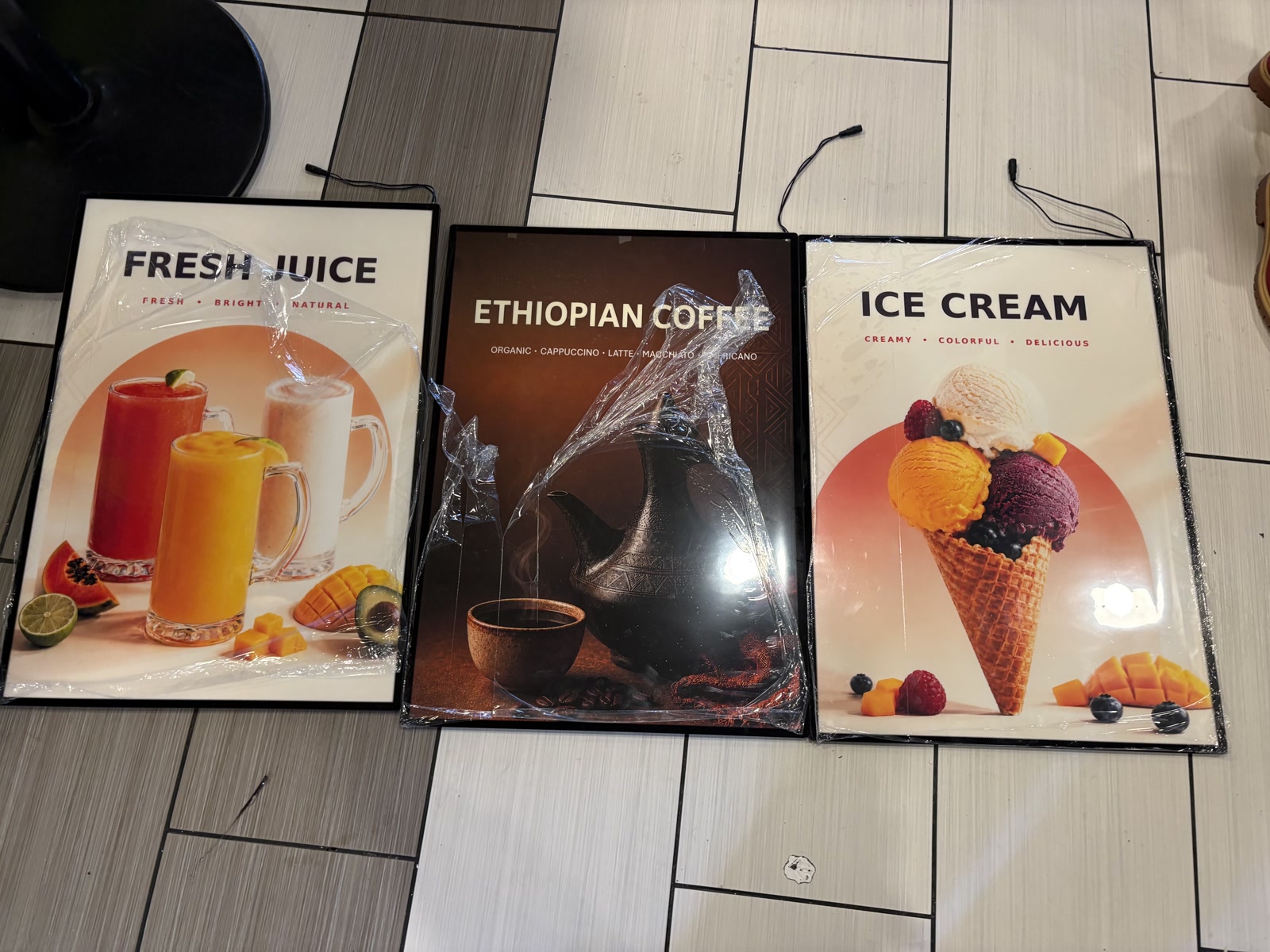 Three framed juice, coffee and ice cream graphics laid out on the floor before installation